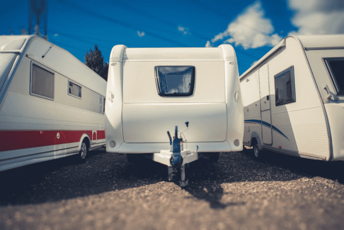 Three white caravans parked side by side under a blue sky. The central caravan has a visible tow bar and a small window on the rear.